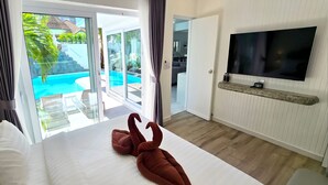 Een hotelkamer met een bed, een televisie, uitzicht op het zwembad en een deur naar een balkon.