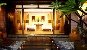 Ein Hotel mit Eingangsbereich und Weg zu einem Zimmer mit zwei Betten, einer Rezeption und tropischen Pflanzen.