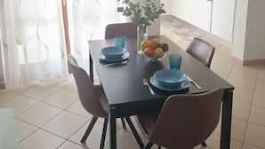 A modern dining area with a table set for two, a vase with fruit, and a kitchen in the background. - A 10-minute walk from Lake Garda, quiet area, a playground 80 m (Raffa)
