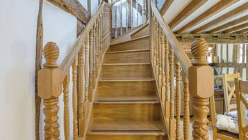 Un escalier en bois doté d’une rampe en spirale, menant à une pièce au plafond haut et aux poutres apparentes.