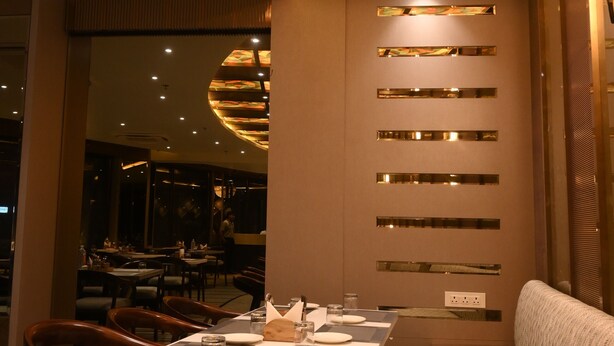 Interior de un restaurante con diseño moderno, que incluye un techo con motivos, una zona de estar con mesas y sillas, y una pared con tiras metálicas horizontales.