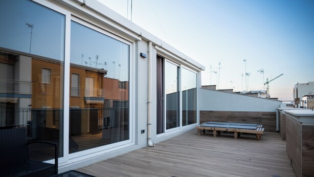 A modern outdoor deck with a wooden floor, glass sliding doors, and a seating area with a table and chairs. - Impulses Home suite Whirlpool (Barletta)