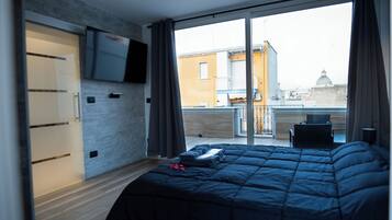 A bedroom with a large bed, a TV mounted on the wall, and a balcony with a chair.
