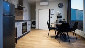 A modern kitchen with a built-in oven, a washing machine, and a dining area with a round table and black chairs. - Impulses Home suite Whirlpool (Barletta)