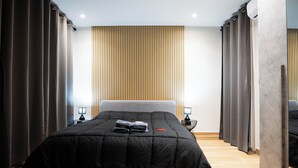 A modern hotel room with a large bed, dark curtains, a wooden slat wall, and a small bedside table with a lamp. - Impulses Home suite Whirlpool (Barletta)