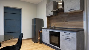 A modern kitchen with grey cabinets, a stainless steel range hood, a built-in oven, and a black refrigerator. - Impulses Home suite Whirlpool (Barletta)