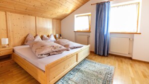 A wooden room with a bed, a nightstand, a window with curtains, and a radiator.