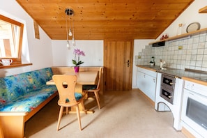 A cozy kitchen with wooden ceiling, a dining area with a bench and chairs, and a tiled backsplash.