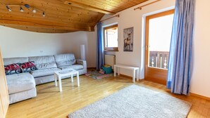 A living room with a wooden ceiling, a sofa, a white coffee table, a rug, and a window with curtains.
