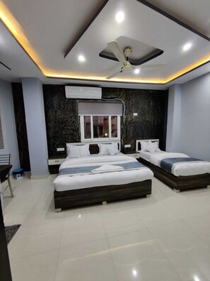 A modern bedroom with two beds, a ceiling fan, recessed lighting, and a large air conditioning unit. - Hotel Nanak Place (Varanasi)