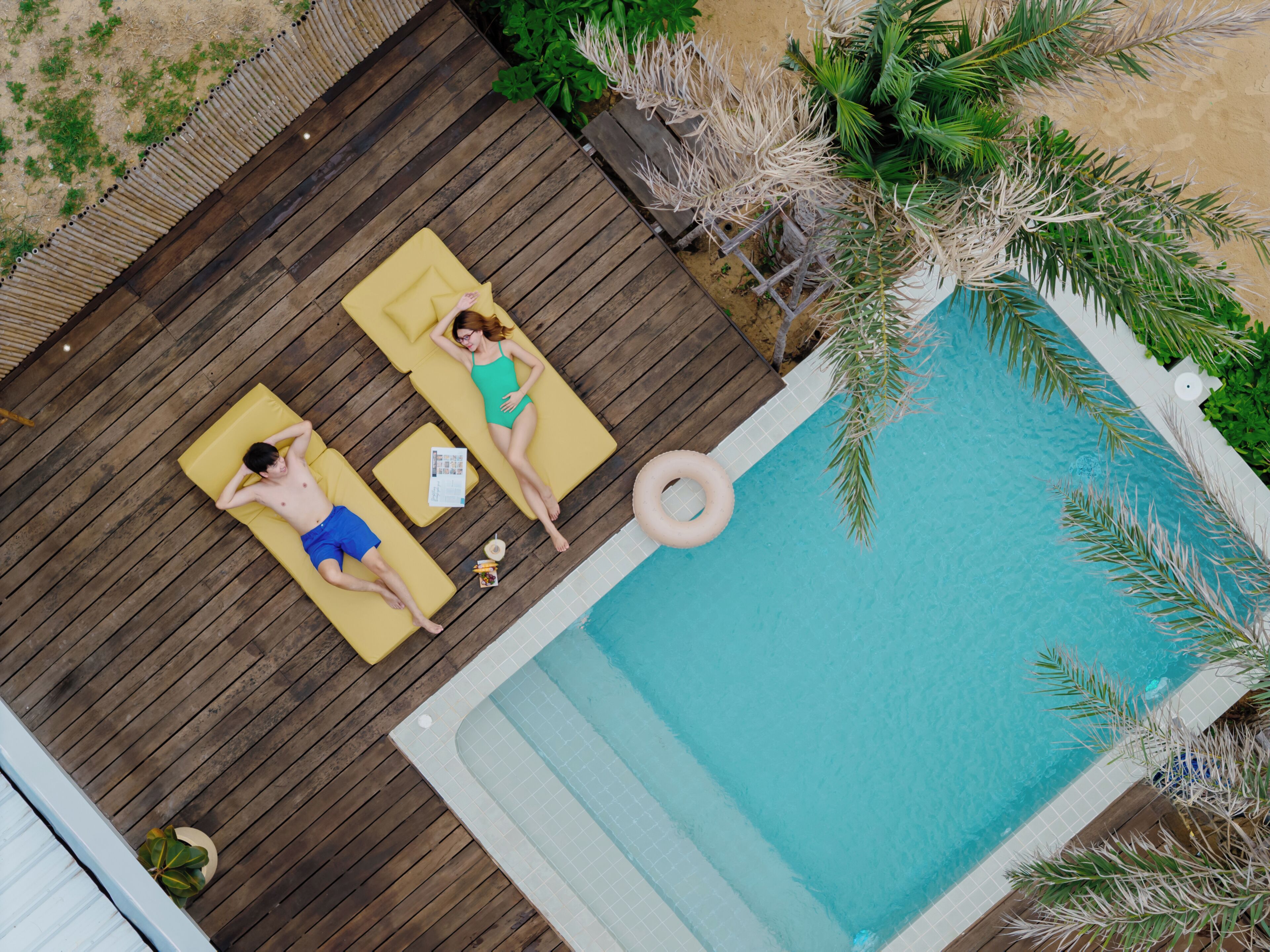 Vue aérienne d’une terrasse en bois avec deux chaises longues, une piscine et la végétation environnante.