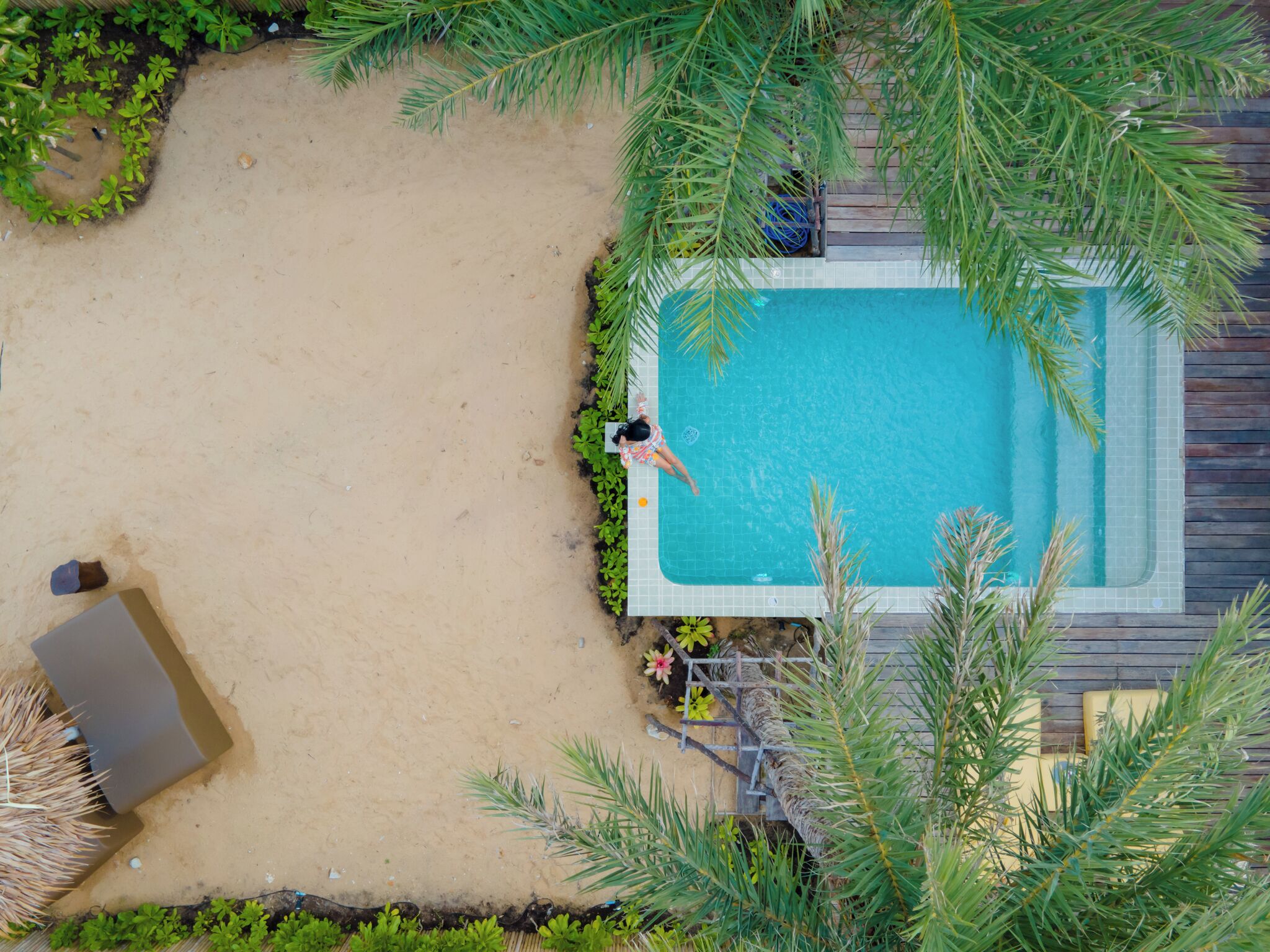 Vista aérea de una piscina rodeada de arena y vegetación, con una persona en el agua.