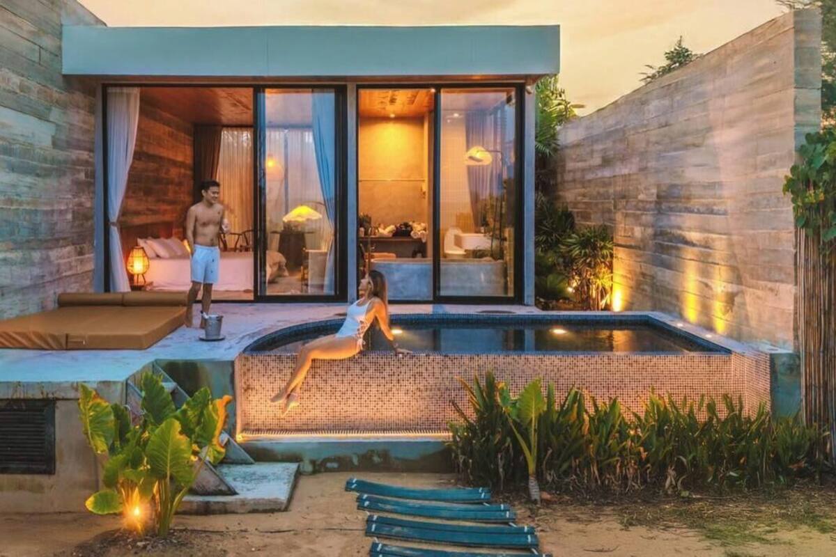 A modern villa with a pool, a guest lounging by the pool, and a person standing by the entrance.