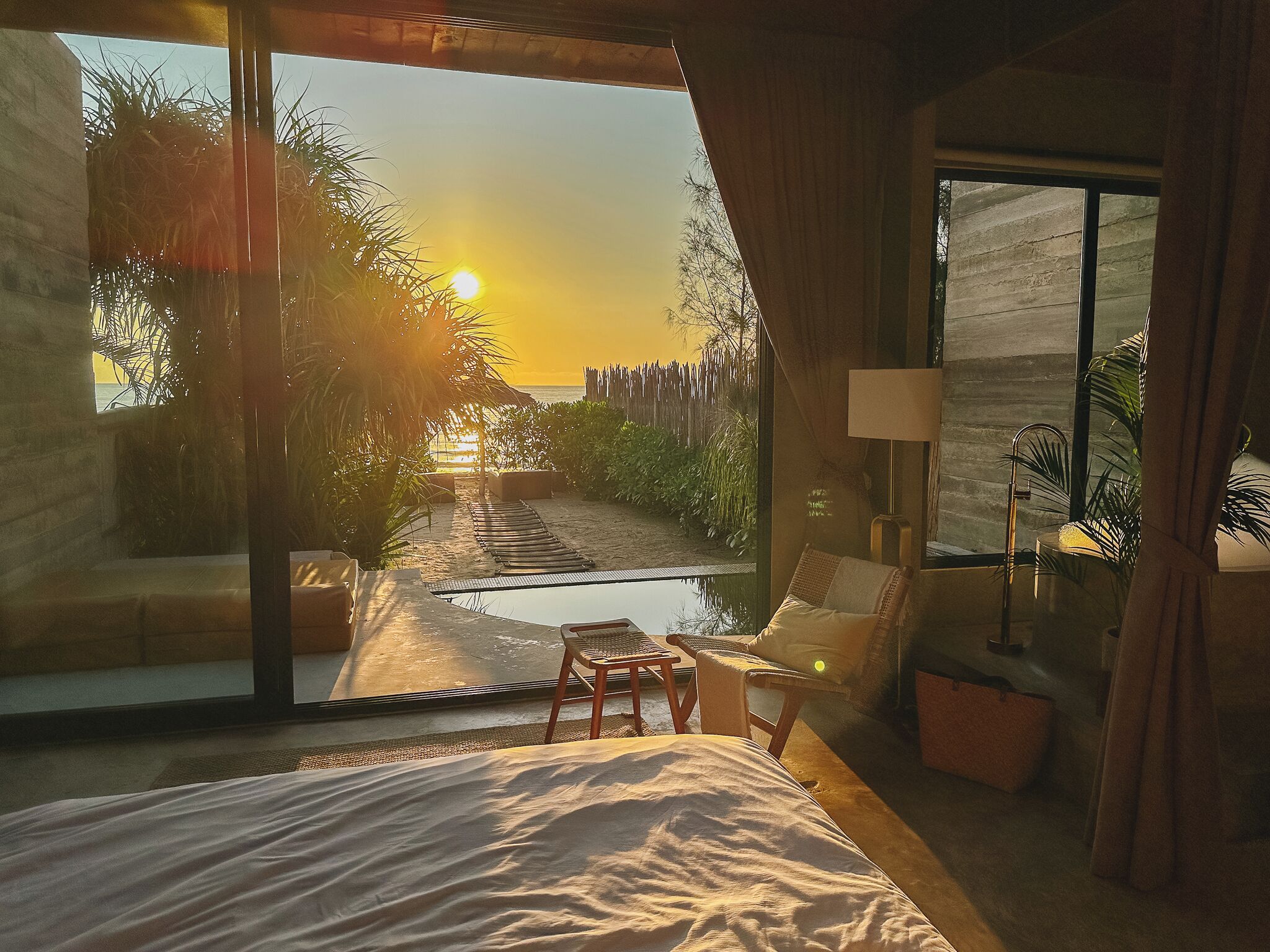 Une chambre avec une grande fenêtre donnant sur une piscine et offrant une vue sur le coucher de soleil.