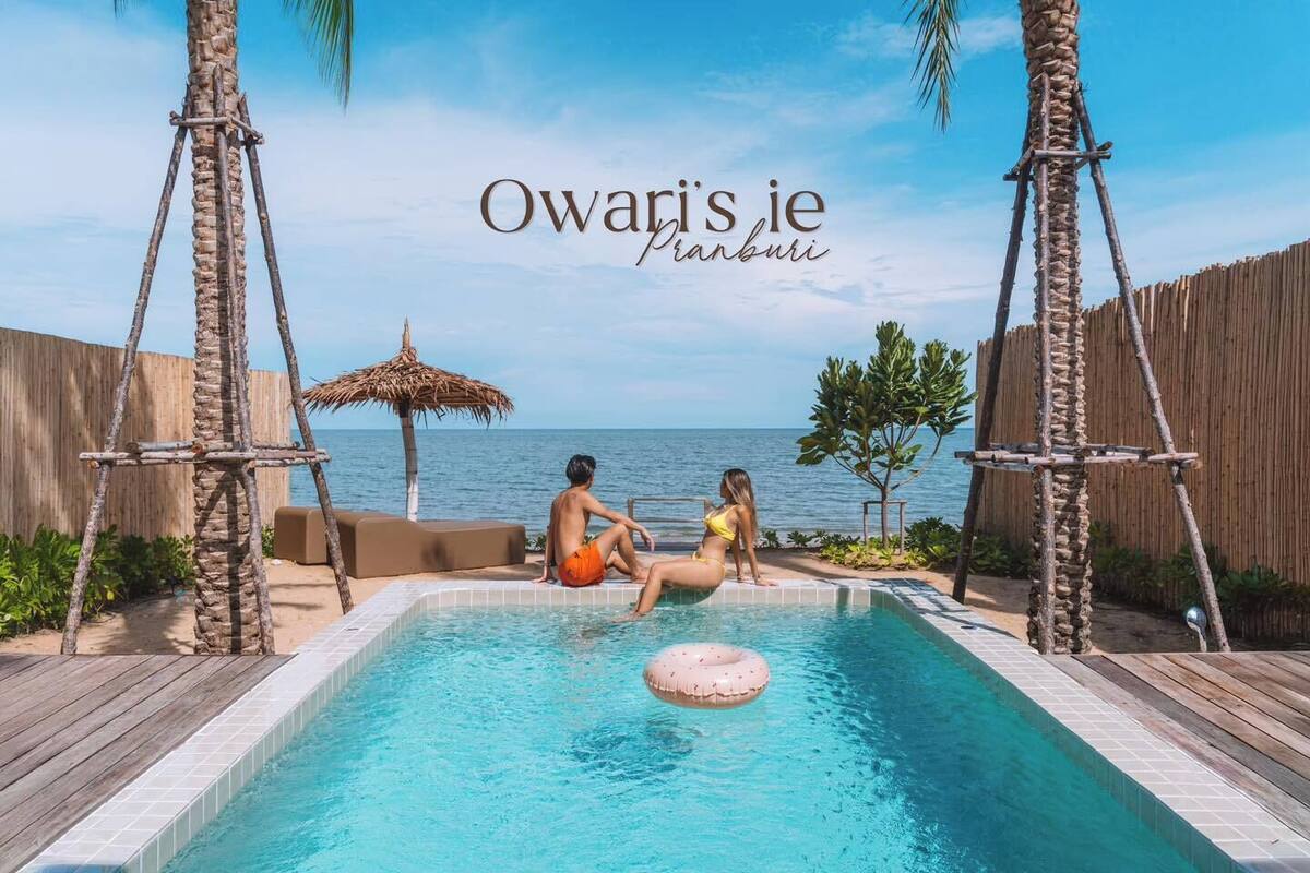 A poolside area with a view of the sea, wooden deck, and a thatched umbrella.