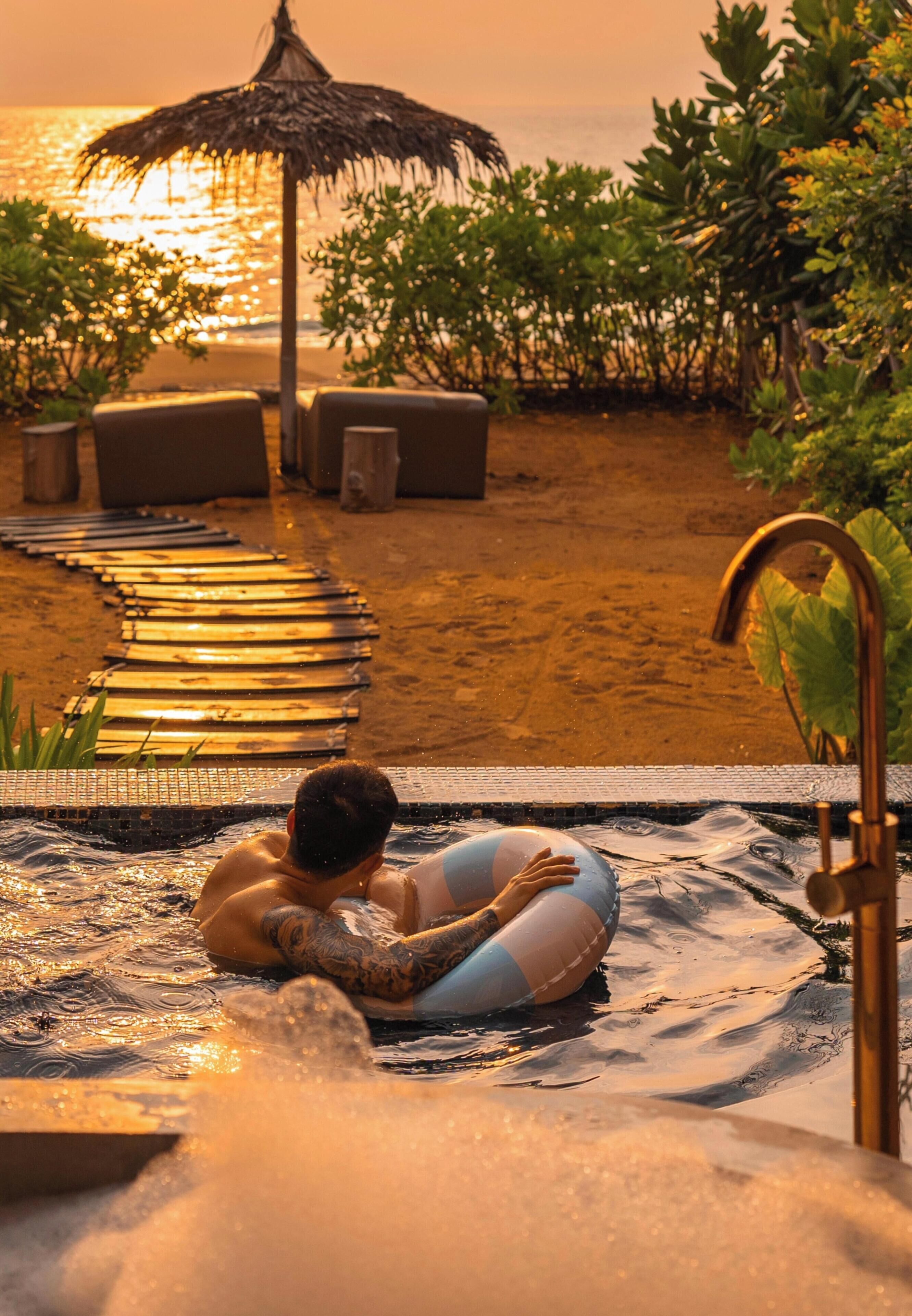 A person in a hot tub with a view of the beach and ocean at sunset.