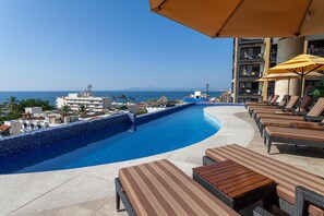 A poolside area with lounge chairs and umbrellas, overlooking a clear blue ocean and a distant shoreline. - Top Views & Signature Comfort - Walk Everywhere 2BD Condo for rent in Amapas, Pu (Puerto Vallarta)