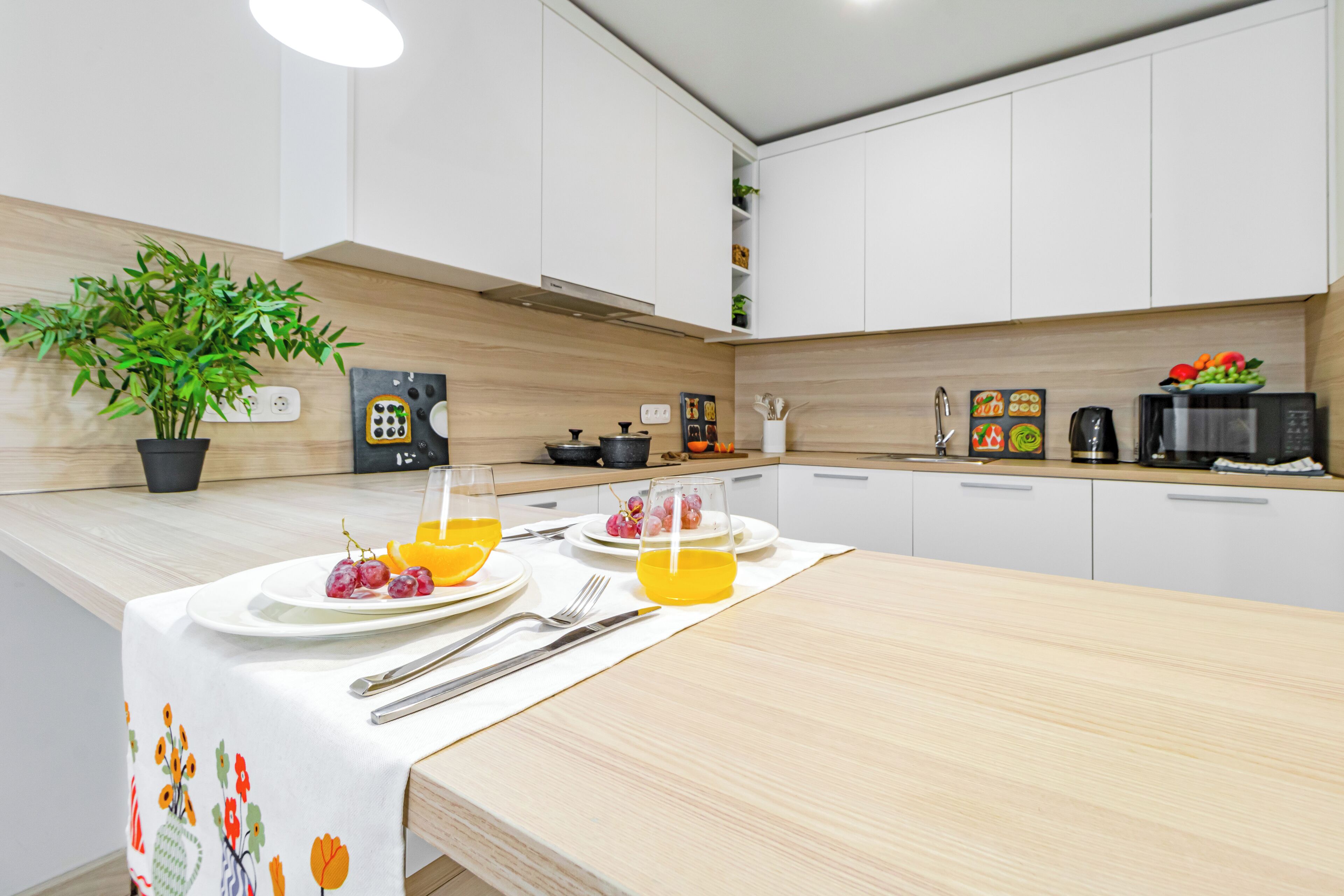 A modern kitchen with white cabinets, a wooden countertop, and a dining area set with plates of fruit and a glass of orange juice.