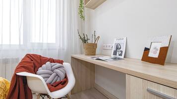 A modern office space with a wooden desk, a white chair, a basket with plants, and framed pictures.