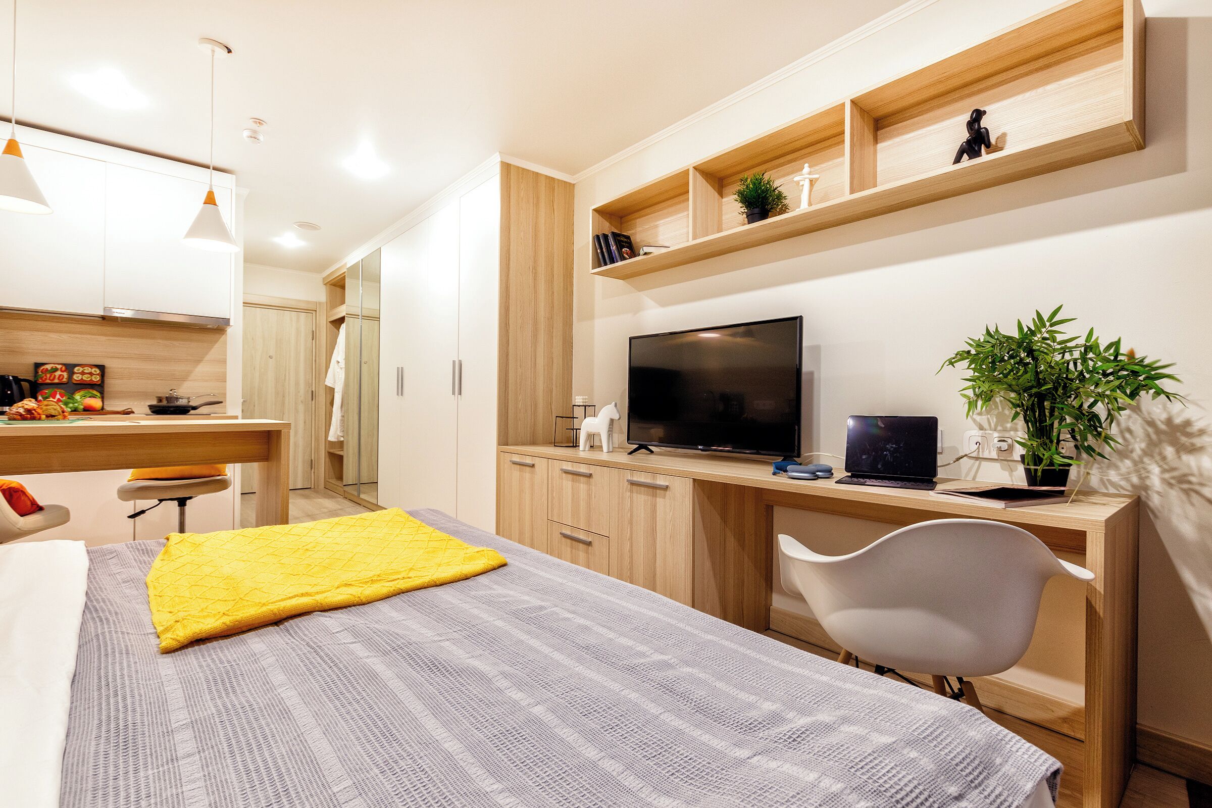 Una camera da letto moderna con un letto, una scrivania, una sedia, una TV e uno scaffale con oggetti decorativi.