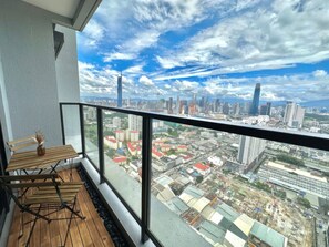 A balcony with a wooden table and chairs, overlooking a cityscape with various buildings and a clear sky.