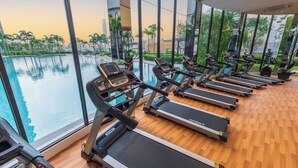 A gym with treadmills and a large window overlooking a pool and palm trees.