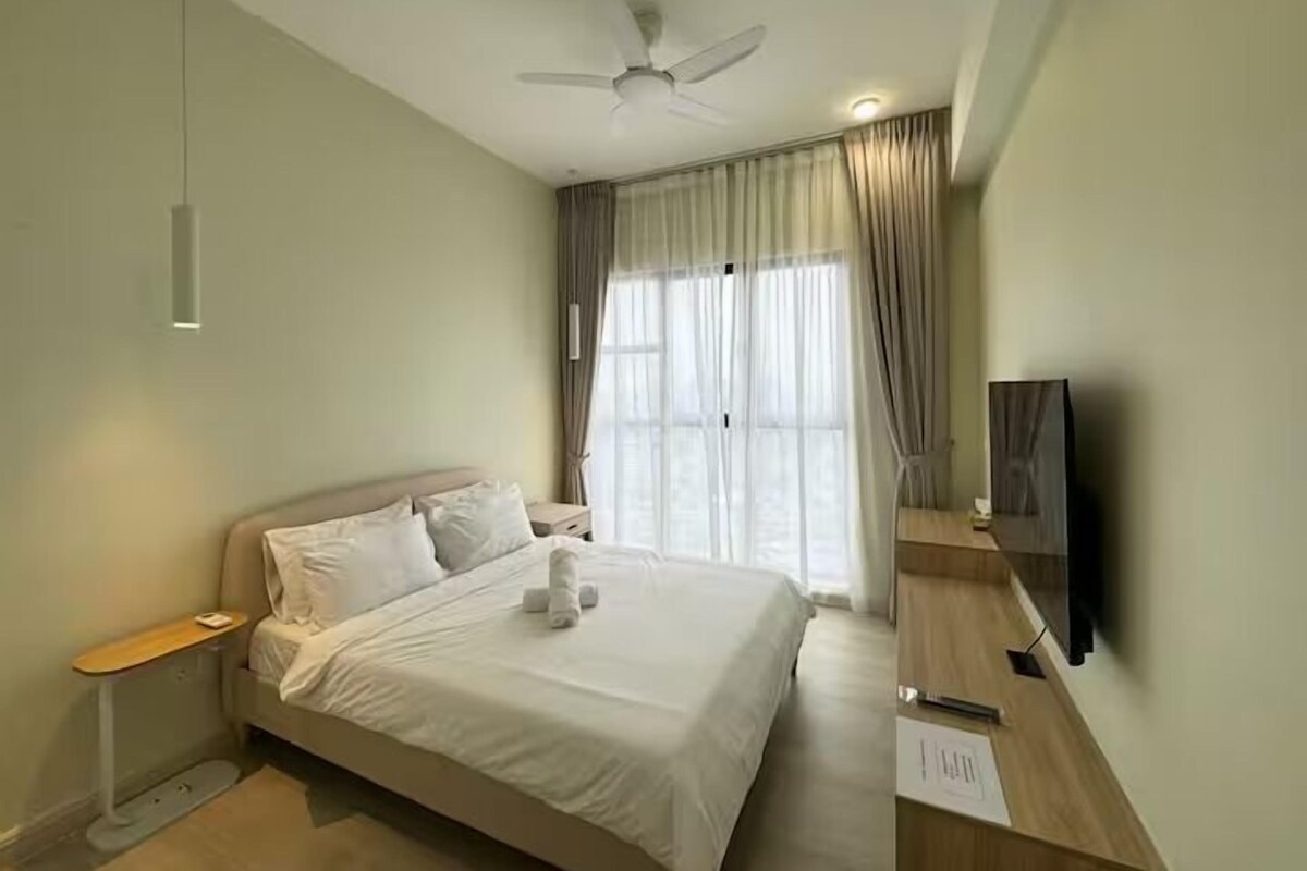 A hotel room with a bed, a ceiling fan, a TV, and a window with curtains.