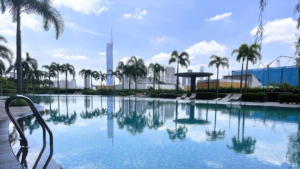 A swimming pool with palm trees, lounge chairs, and a modern building in the background.