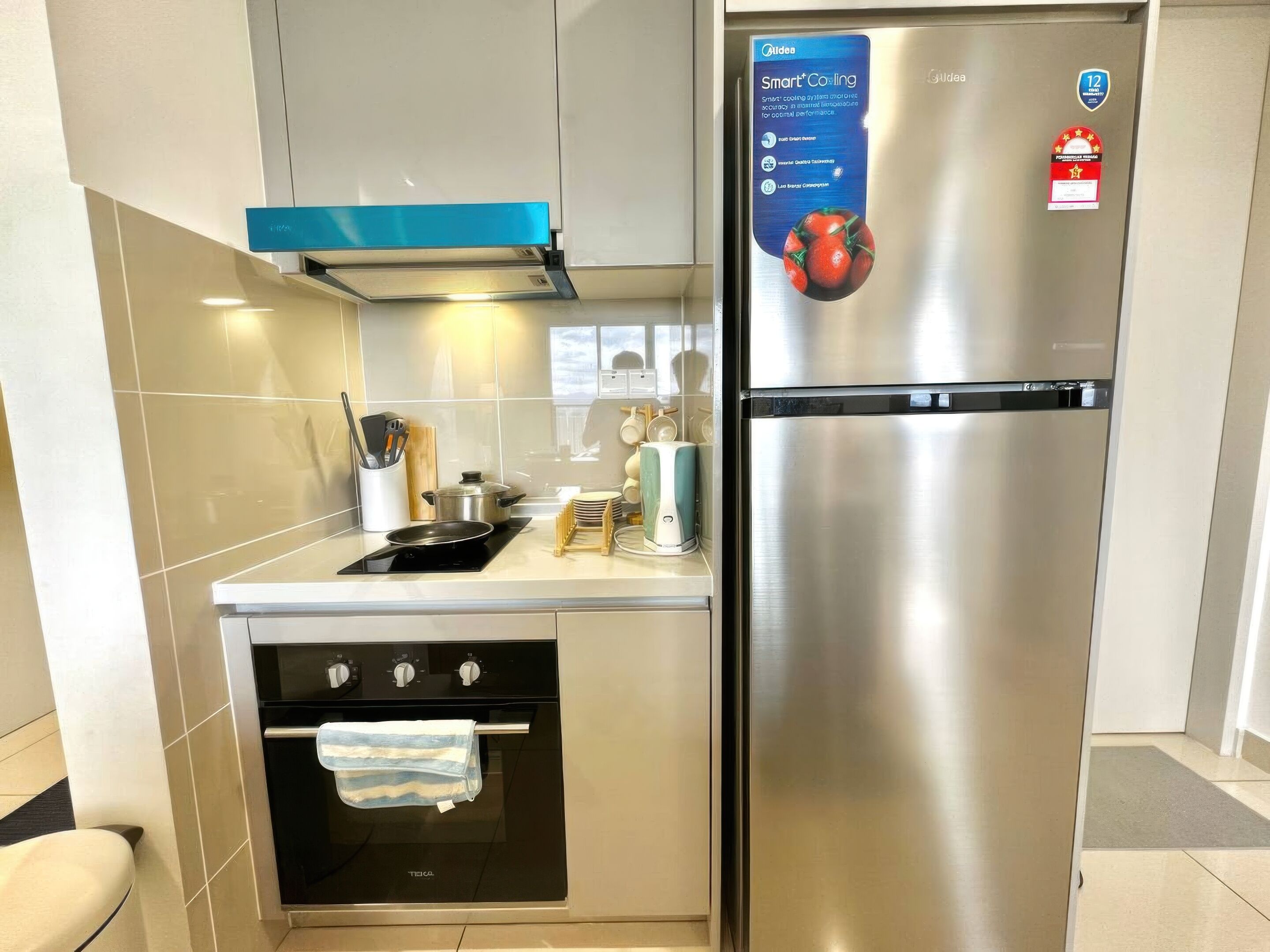 A compact kitchen with a stainless steel refrigerator, a built-in oven, and a blue range hood.