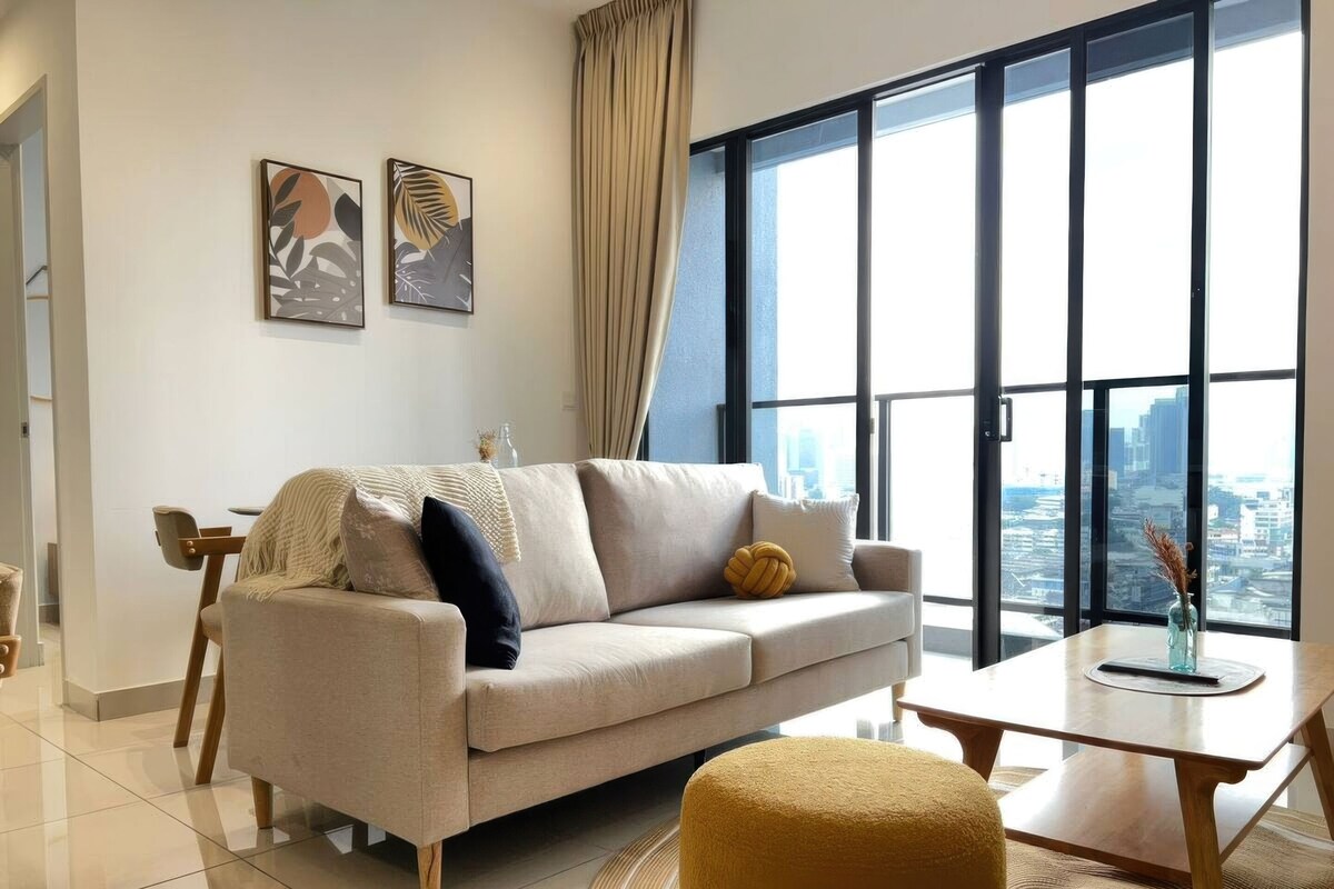 A modern living room with a sofa, a coffee table, and a view of a cityscape through large windows.
