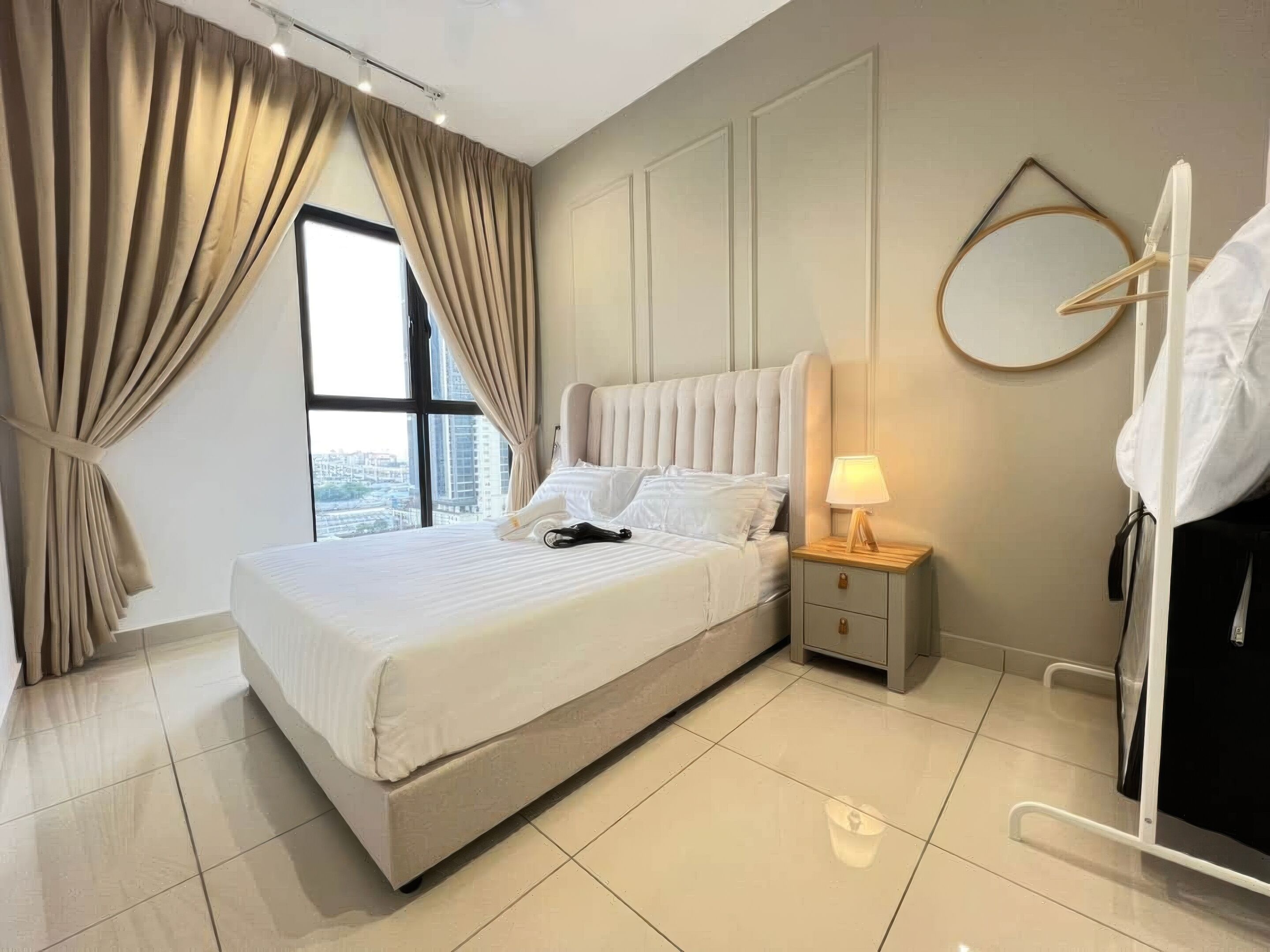 Une chambre d’hôtel avec un grand lit, une table de chevet avec une lampe, une armoire et une vue sur la ville par une fenêtre avec des rideaux.