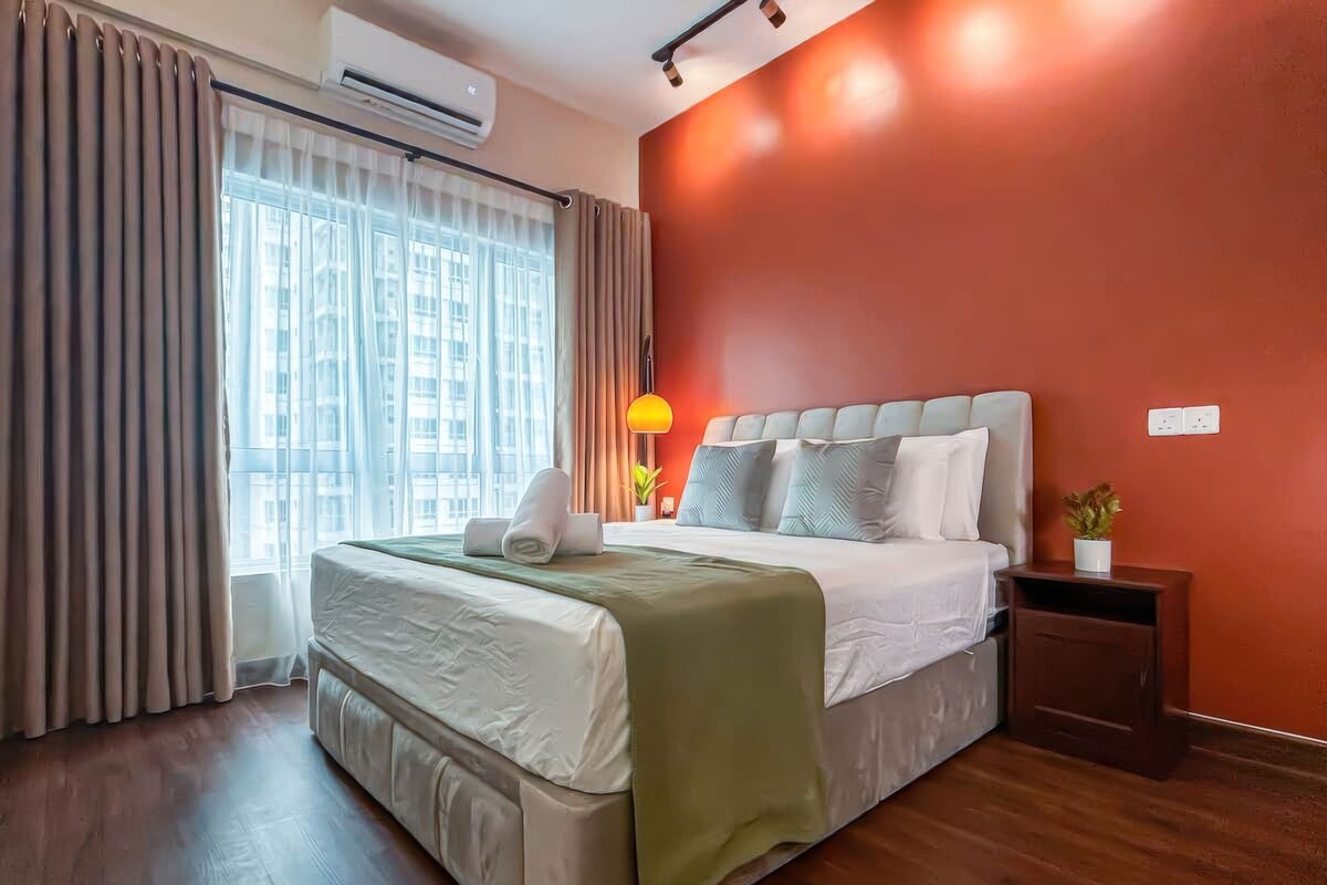 A hotel room with a bed, a nightstand, a lamp, and a window with curtains.