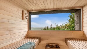 Un sauna avec des bancs en bois, une fenêtre donnant sur la mer et un foyer au centre.