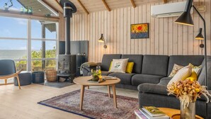 Un salon chaleureux avec un canapé, une table basse et une cheminée. Une grande fenêtre offre une vue sur l’extérieur.
