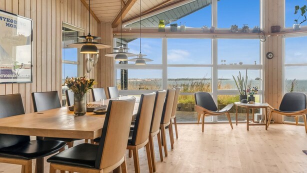 Un vaste espace dédié à la salle à manger, avec une grande table et des chaises en bois, de grandes fenêtres donnant sur l’extérieur et un éclairage suspendu.