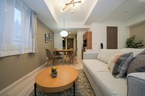 Una sala de estar moderna con una mesa de centro redonda de madera, un sofá color beige y un comedor con una mesa y sillas de madera.