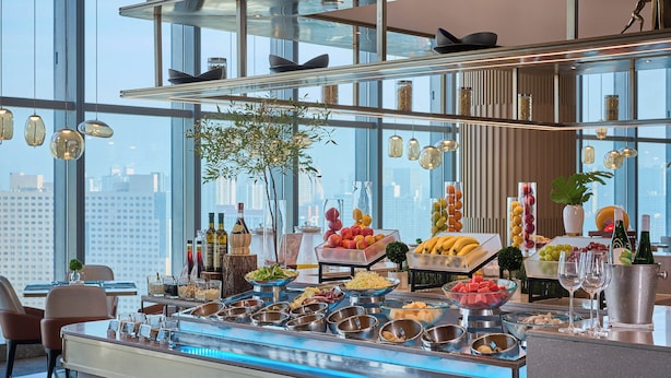 A buffet with various food items and drinks, a large window with a city view, and modern interior design. - MaxX Harbour-view Qingdao (Qingdao)