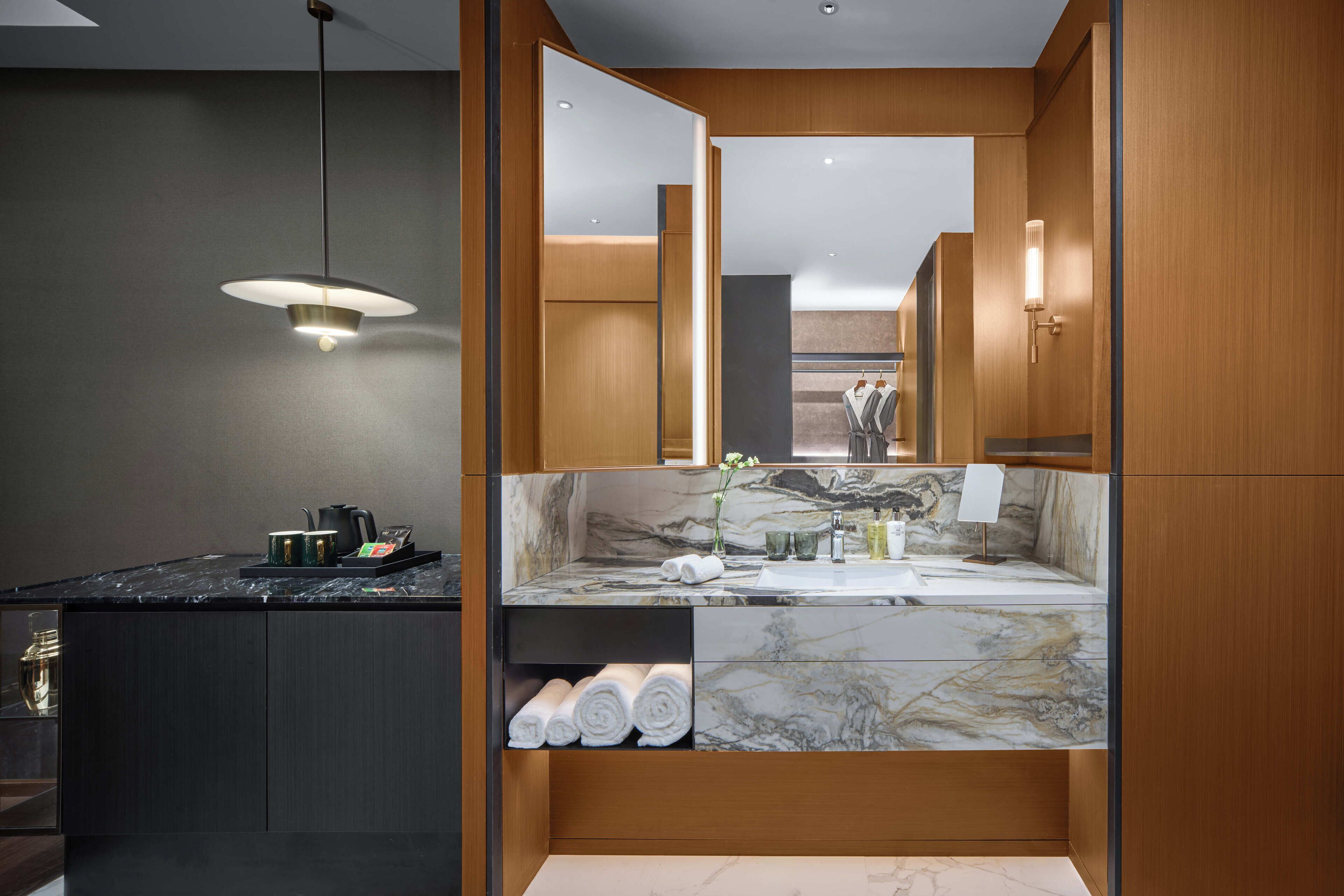 A modern bathroom with a marble vanity, wooden cabinetry, and a hanging light fixture.