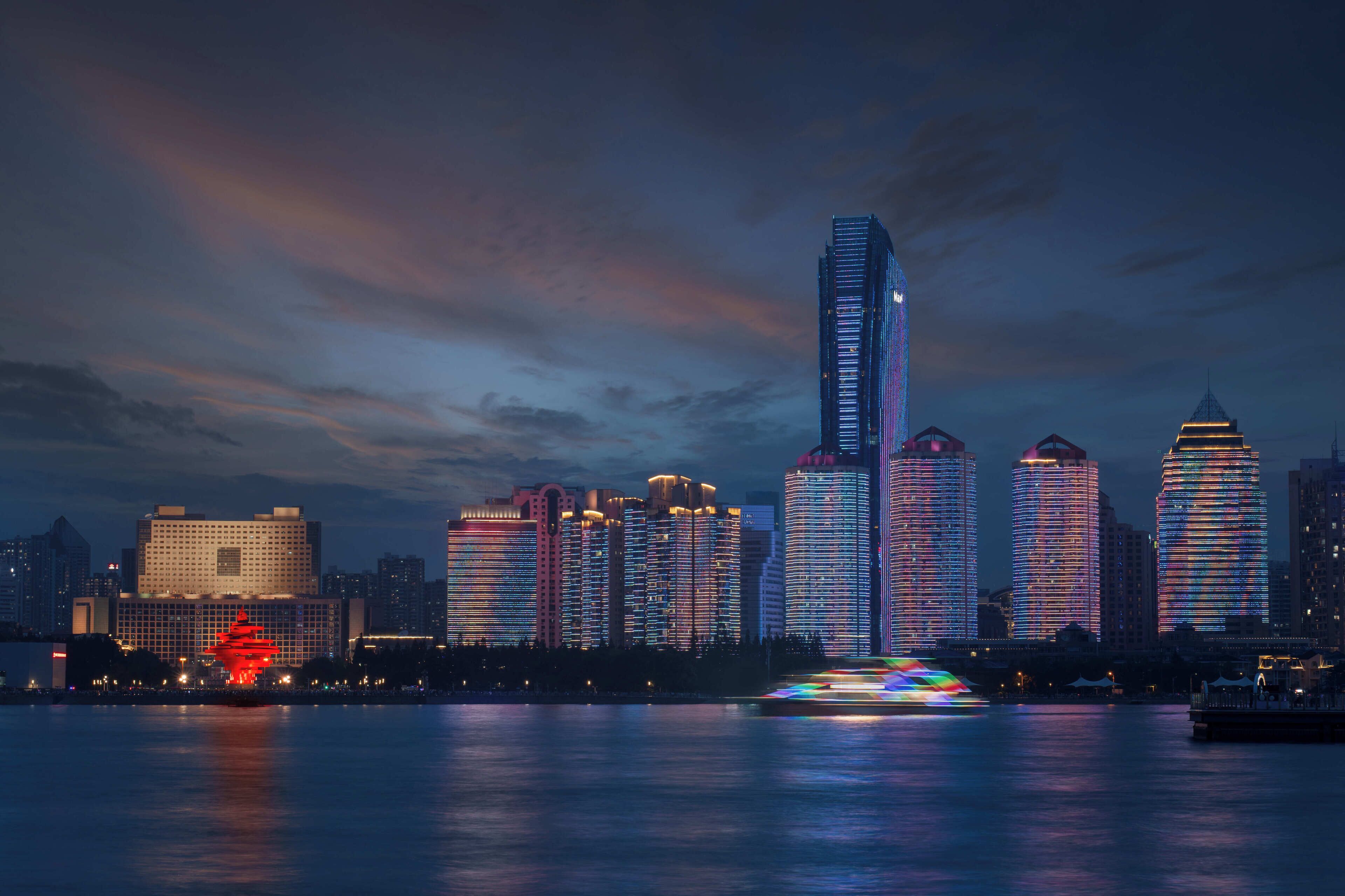 Un horizonte urbano al anochecer con edificios iluminados y su reflejo en el agua.