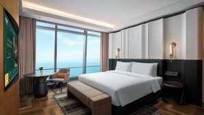 A modern hotel room with a large bed, a desk, a chair, and a view of the ocean. - MaxX Harbour-view Qingdao (Qingdao)