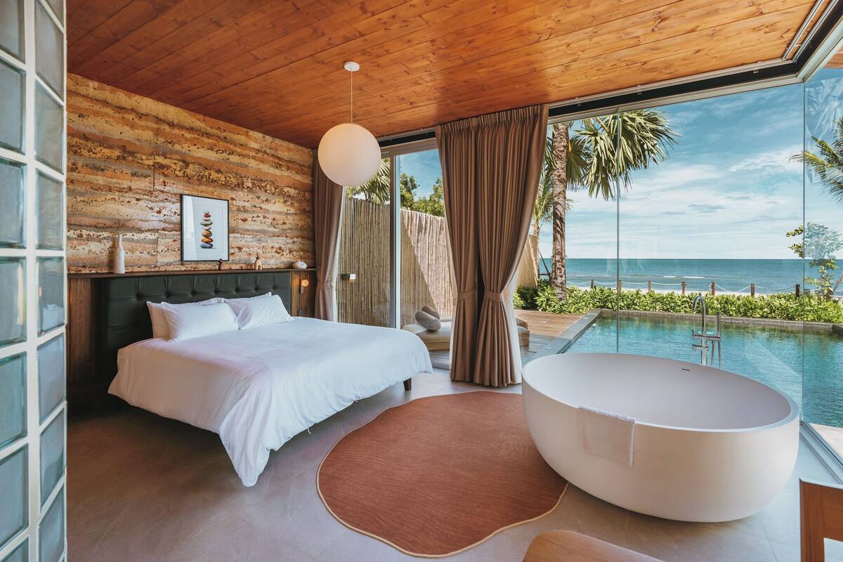 A bedroom with a large bed, a bathtub, and a view of the ocean.