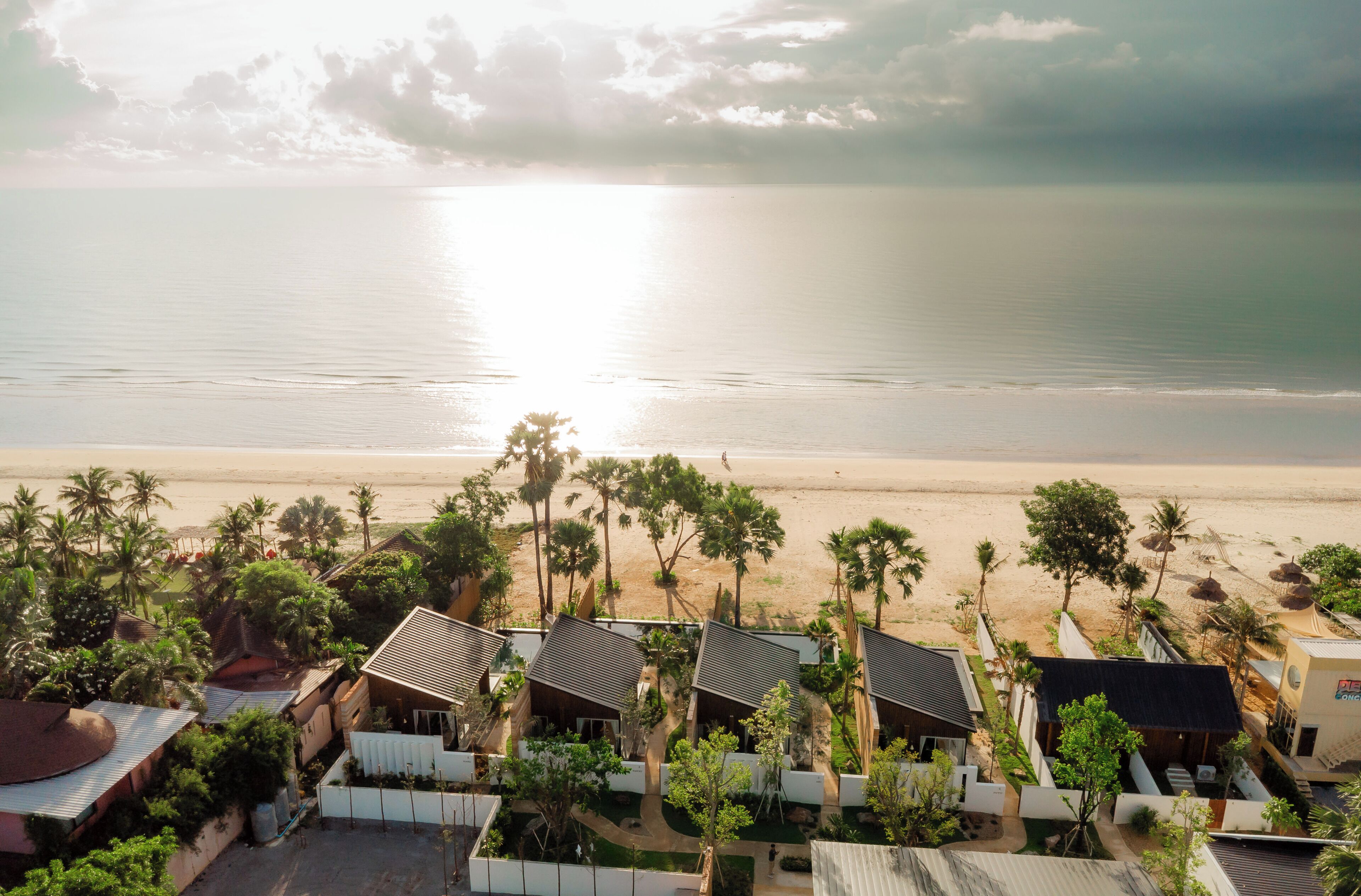 A beachfront property with multiple bungalow-style buildings, a sandy beach, and palm trees.