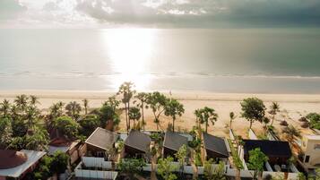 A beachfront property with multiple bungalow-style buildings, a sandy beach, and palm trees.