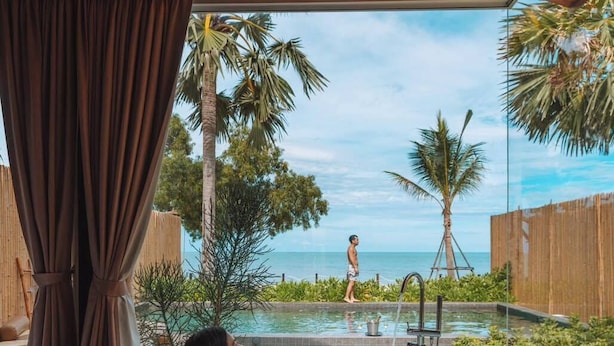 A woman relaxing in a large bathtub with a view of a pool and palm trees. - Furusato Shack (Pranburi)