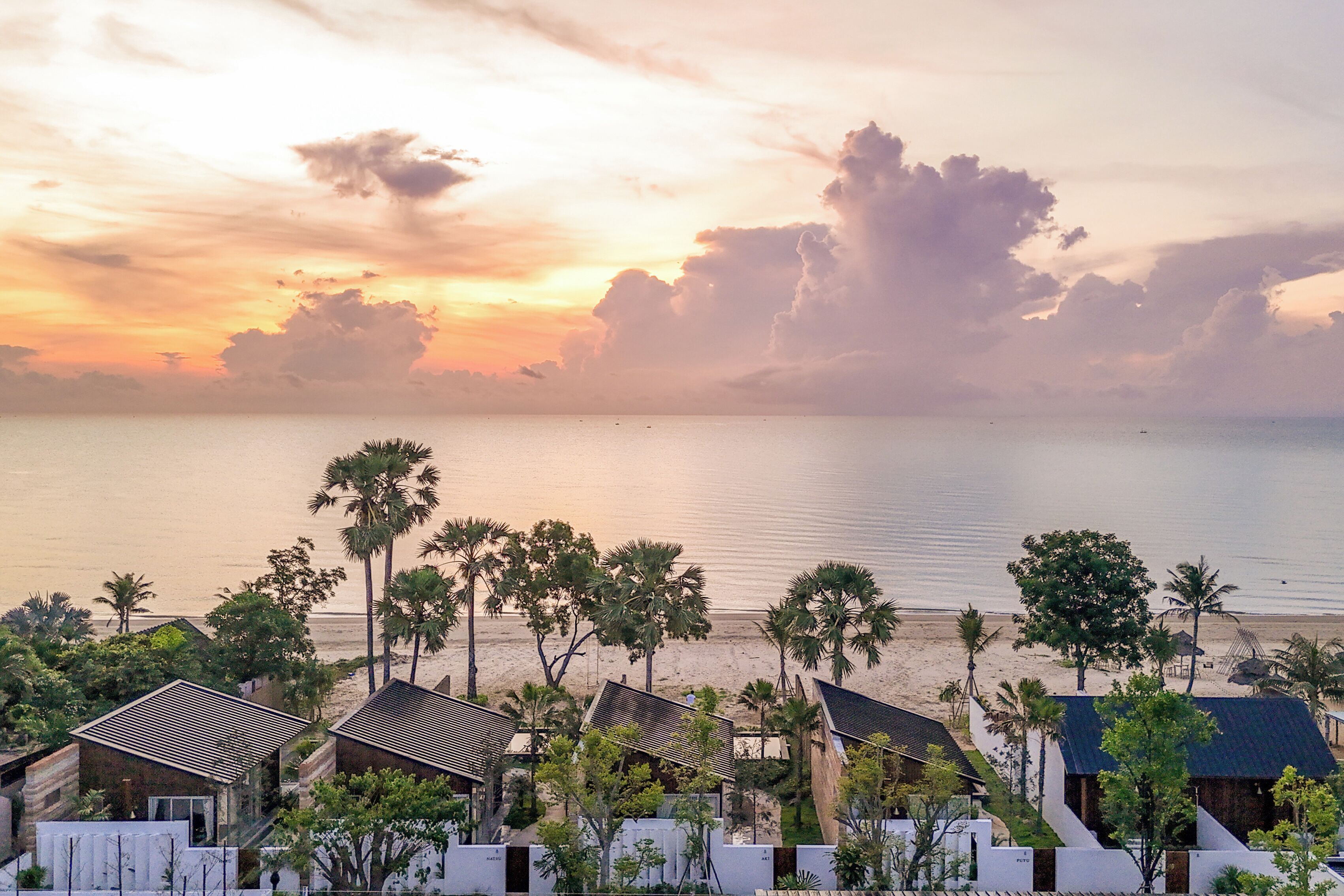 A coastal hotel with multiple buildings, palm trees, and a beach view.