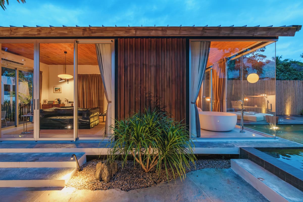 A modern house with a glass door leading to a living room with a sofa and a dining area.