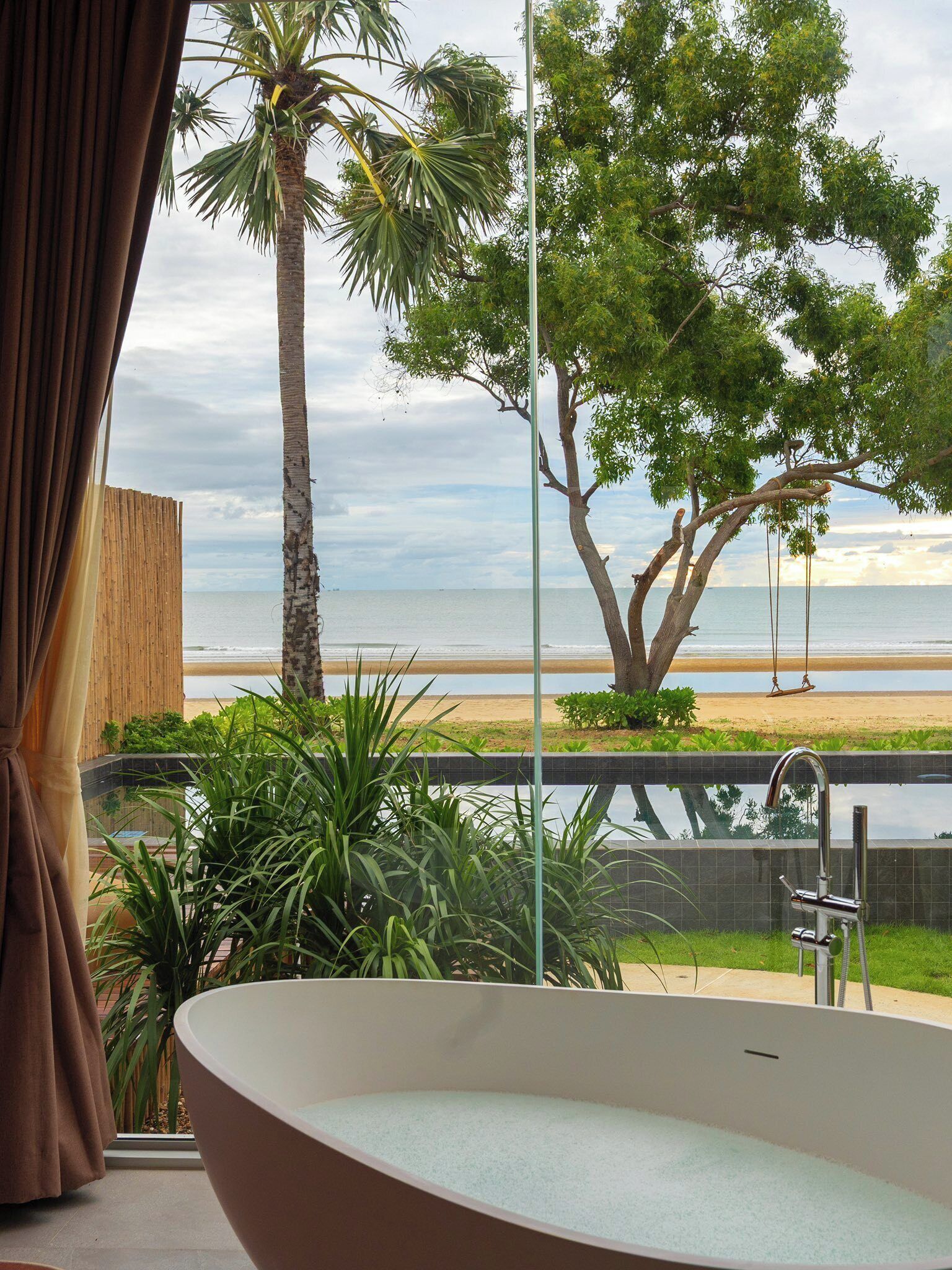 A bathroom with a large bathtub, a view of the beach, and a swing in the background.