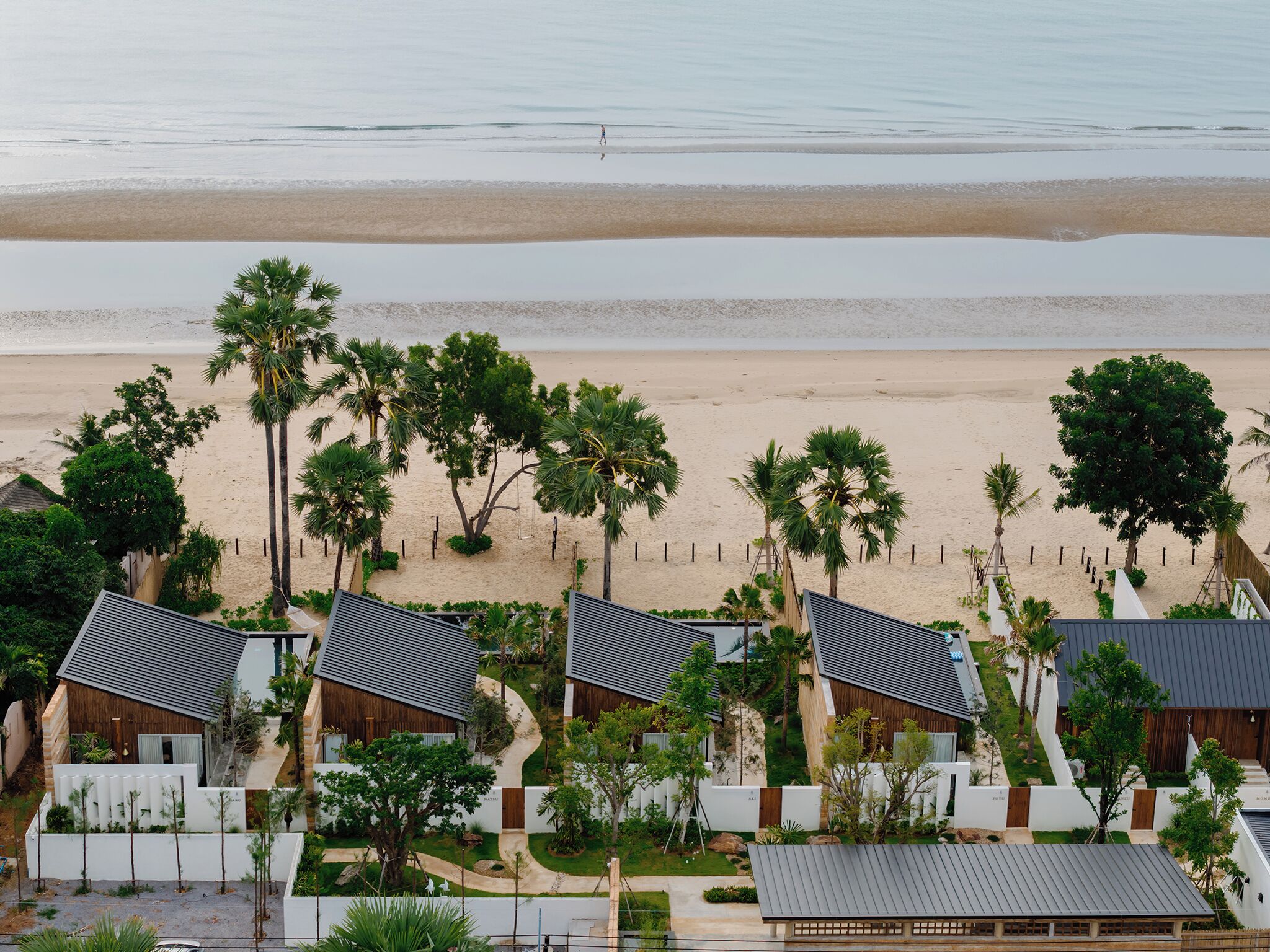 A beachfront resort with multiple bungalow-style buildings, palm trees, and a sandy beach.