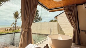A bedroom with a large window, a bathtub, and a view of the beach. - Furusato Shack (Pranburi)