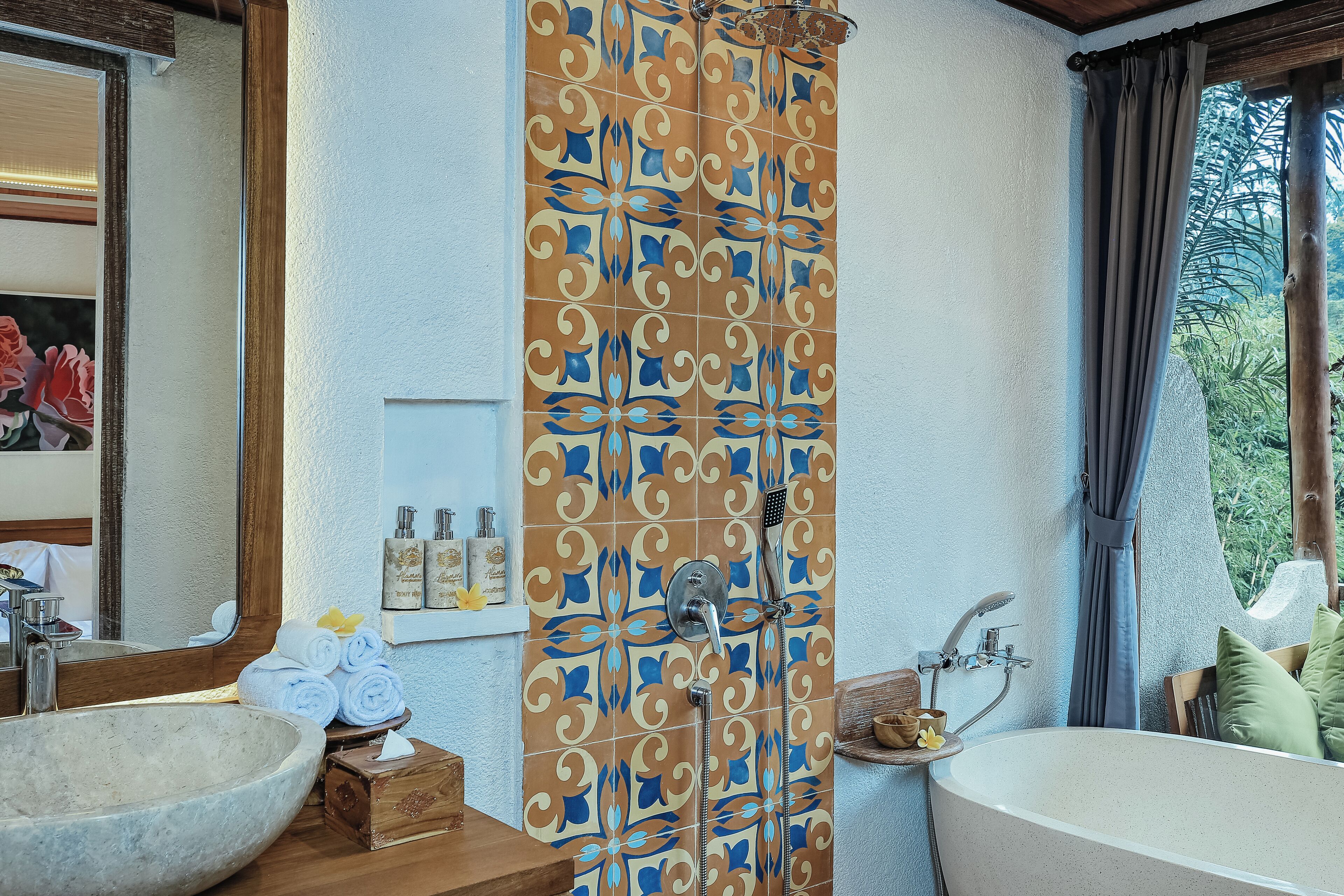 A bathroom with a large stone sink, a bathtub, and a shower with a patterned curtain.
